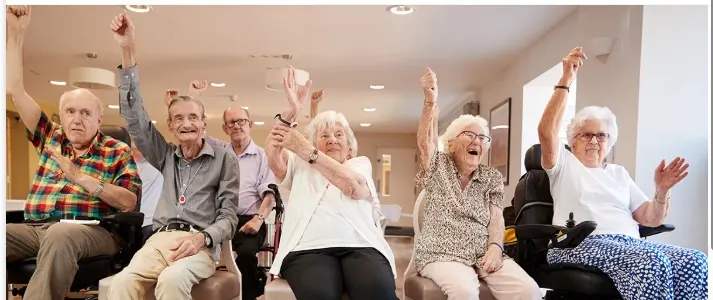 Un grupo de personas mayores, sentadas, levantan los brazos y ríen mientras bailan